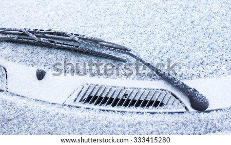 Wiper and windscreen of the parked car covered with snow. Close-up.