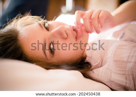 closeup portrait of romantic beautiful young woman green eyes sensual girl with big lips in shirt having fun touching herself posing relaxing lying on a white bed & looking at camera