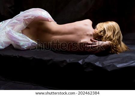 picture of young woman blond pretty girl having fun posing half nude lying on black stage with beautiful sexy back to camera in white valance touching herself sensually on copy space background