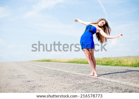 exciting flying like bird: portrait of beautiful brunette young woman having fun walking on the road on blue sky outdoors copy space background