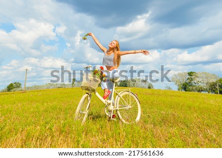 freedom cycling: portrait of beautiful blonde young woman having fun enjoying summer cycling with hands up and happy smiling on green summer outdoors copy space background
