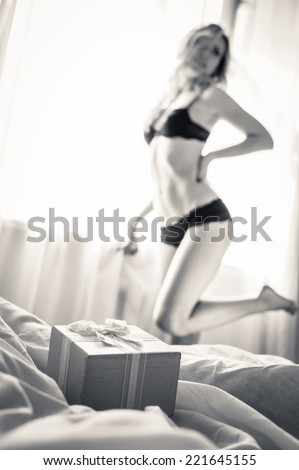 closeup on pink gift box present with one elegant blonde pinup pretty female in underwear having fun posing relaxing standing on light copy space background, black and white portrait