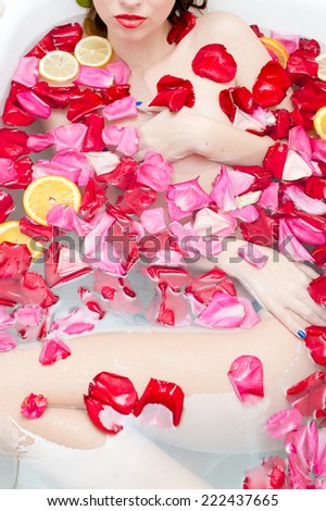 luxury spa queen: beautiful sexy elegant young lady with red lipstick & silk skin having fun lying in water bath relaxing on colorful rose petals copy space background
