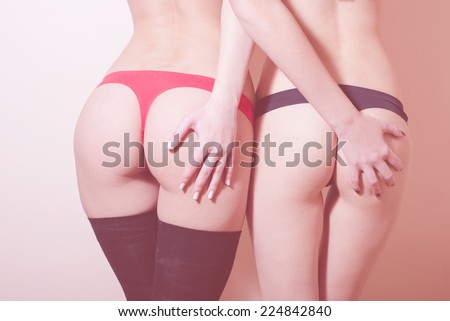 hands on sexy bums: close up image of 2 glamor girlfriends young women having fun posing showing their beautiful buttocks in black & red lingerie on light copy space background
