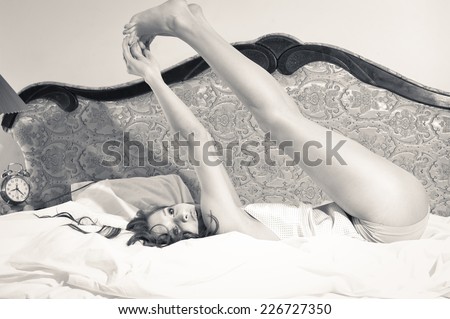 joyful morning: black and white portrait of beautiful gorgeous young lady having fun relaxing lying in lingerie on white bed and sensually looking up on a light copy space background