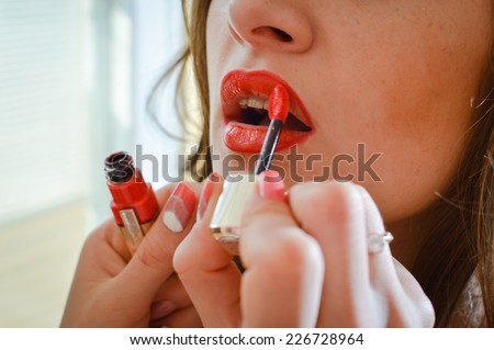 red lipstick: makeup artist hands draws glamor charming beautiful girl lips, closeup image