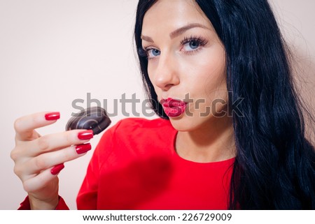 closeup portrait of luxury funny pretty lady with seductive lips and red manicure nails eating chocolate cake or marshmallow and looking at camera on light copy space background