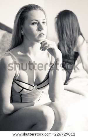 black and white picture of 2 gorgeous sexy pinup girlfriends sitting together in bed on light copyspace background