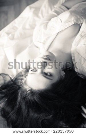 dreaming beauty: black and white closeup portrait of young beautiful glamor woman in white shirt relaxing lying on the bed