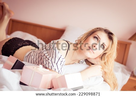 enjoying pink presents in bed: romantic sexy blond young lady having fun relaxing lying in white bed happy smile on light copy space background