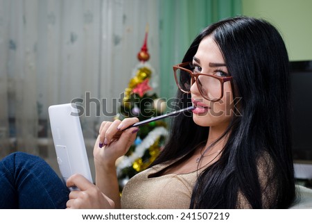 portrait of sexy pretty girl in glasses holding a tablet pc computer relaxing sitting on chair & flirty looking at camera