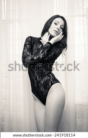 portrait of young pretty lady with perfect fit body in black combies dress standing on light curtain copy space background