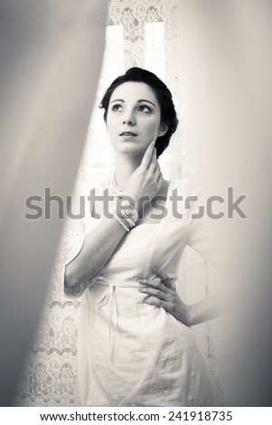 elegant beautiful young lady in white dress hiding in tulle curtain on copy space background, black & white portrait