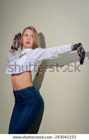 Blonde pretty girl in black transparent gloves, shirt and jeans posing on copy space wall