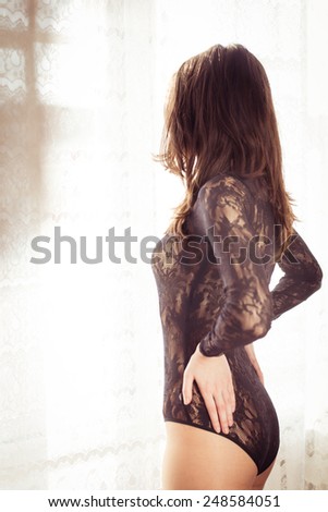 portrait of young beautiful lady with perfect fit body in black combies dress standing on light window curtain copy space background
