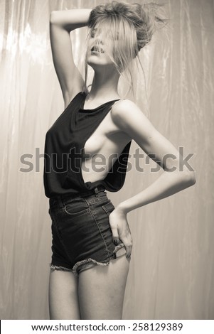Black and white portrait of sexy beautiful young lady in black top and jeans shorts on light curtain background
