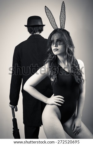 Black and white image of sexy beautiful young lady wearing bunny ears posing over male silhouette on light copy space background