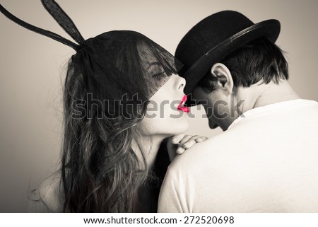 Black and white image of sexy beautiful young lady wearing bunny ears whispering to man in hat on light copy space background