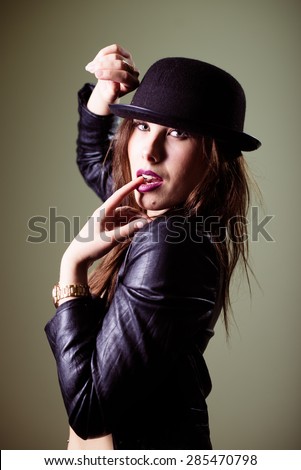 Close up portrait of hot sexy pretty young lady wearing black hat and leather jacket sensually looking at camera on gray copy space background