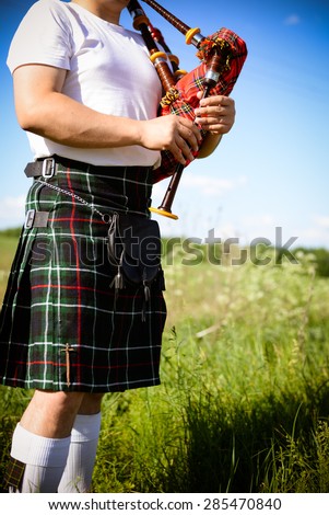 Image close up of man enjoying playing pipes in Scotish traditional kilt on green outdoors copy space summer field