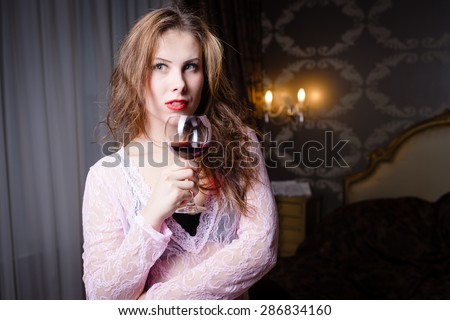 Portrait of beautiful young lady with a glass of wine on luxury bedroom background