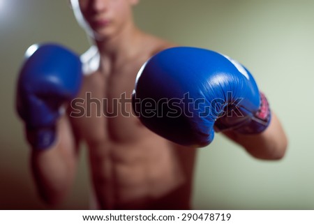 Young man training box punches with blue gloves closeup on strong muscles of torso over dark studio background