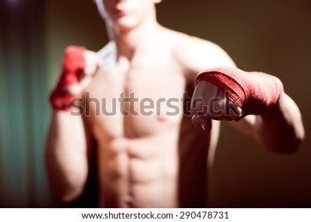 Young man training box punches with bandages closeup on strong muscles of torso over dark studio background