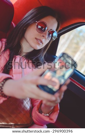 Portrait of beautiful young woman making self picture on the mobile phone in luxury car