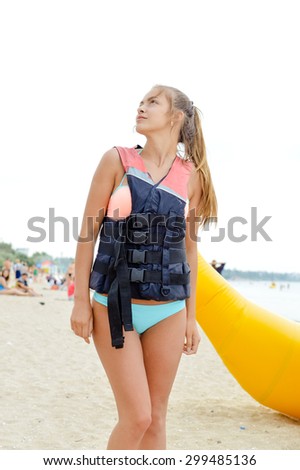 Young blond female with pony tail  in life jacket on beach