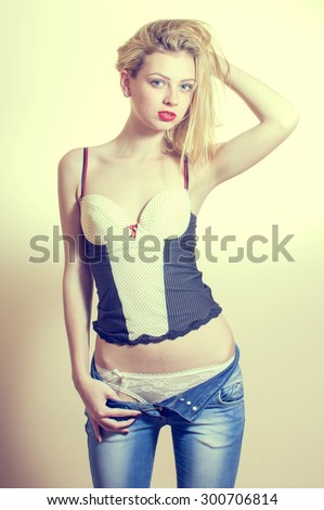 Gorgeous young blonde lady having fun showing her excellent fitness slim body undressing jeans on light background copy space