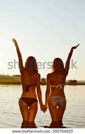 Picture of two sexy best girlfriends in bikini having fun together holding hands up to sky on summer sunset outdoors copy space background