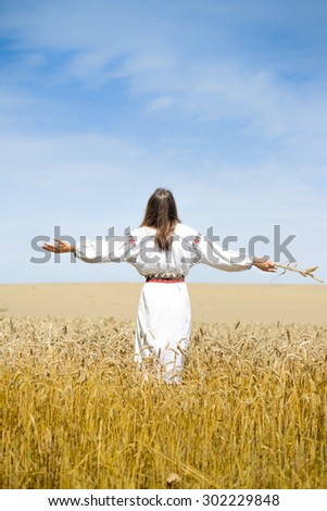 Picture of female in traditional dress standing hands up to sky relaxing in wheat field on summer day background outdoors