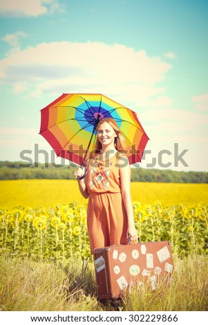 Picture of pretty female holding rainbow umbrella and travel suitcase on the sunflower field outdoors copy space background