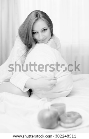 Black and white portrait of beautiful sexy blonde young lady lying on white bed and happy smiling on light background copy space