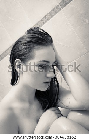 Black and white closeup portrait of looking depressed and crying emotional blond young naked pretty woman taking shower