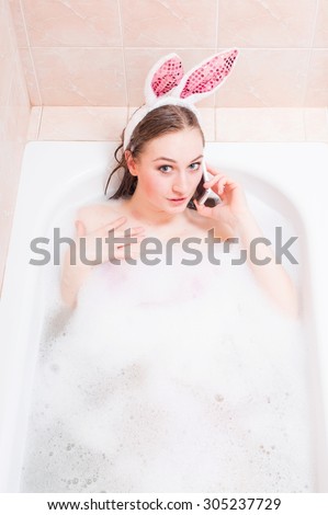 Portrait of wearing funny bunny ears and talking on phone beautiful funny sexi pinup girl over soap water copy space background