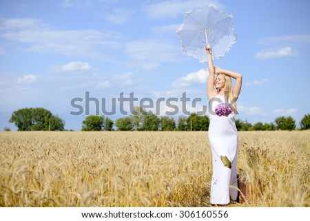 Full length picture of beautiful  blond young female  with umbrella up in air standing in field of golden wheat looking away copyspace.