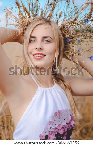 Closeup portrait of perfect smiling young blond lady with wheat spikelets behind her head holding arms up over rural background looking at camera