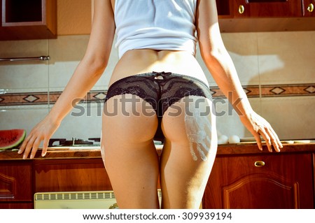 Closeup picture of sexy female model wearing black lace panties in kitchen. White flour handprint on hip.