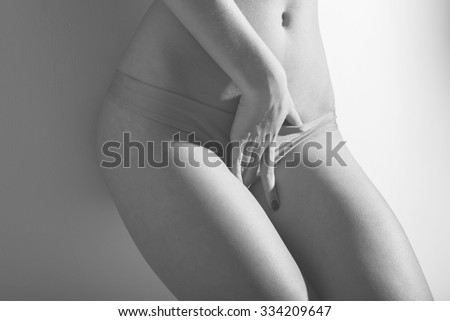 Image closeup of sexy glamor young lady having fun posing near wall showing her body fitness hips in lingerie on light copy space background. Black and white photography