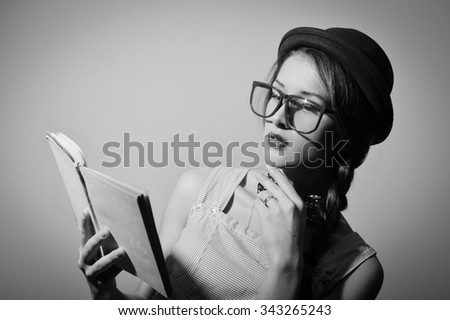 Portrait of beautiful young female in hat and glasses reading a book. Black and white photography