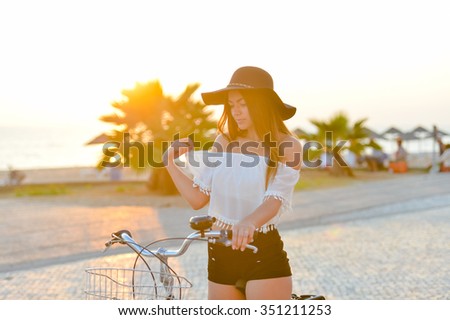 Photo of excited lady in black hat and white top spinning bicycle pedals in summer on sea embankment background
