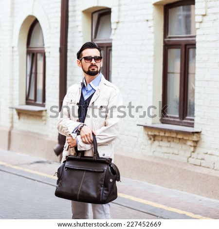 Young urban businessman on smart phone running in street wearing jacket and leather bag