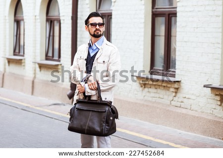 Young urban businessman on smart phone running in street wearing jacket and leather bag