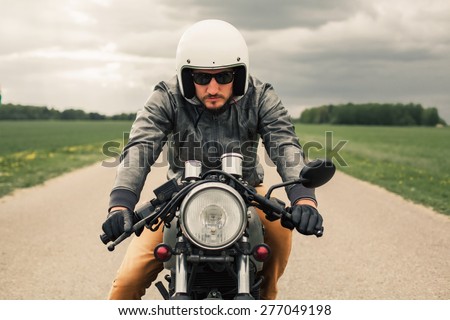 Hipster man driving vintage style cafe-racer motorcycle on the road