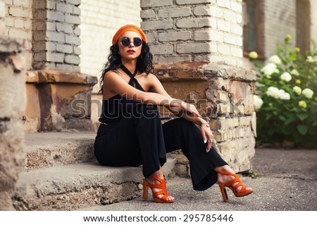 beautiful young girl in the orange hat and sunglasses walks down the street in the summer