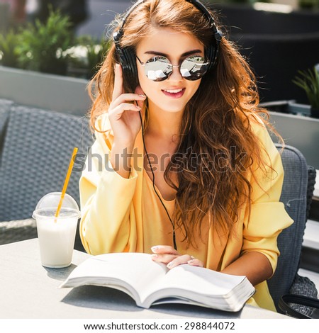 young beautiful woman sitting in a cafe reading a book listening to music and drinking a milkshake
