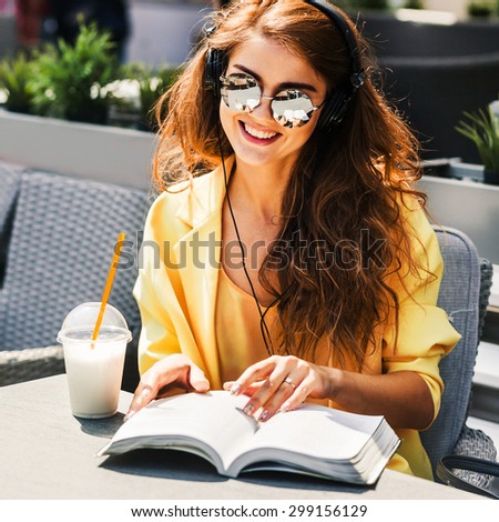 young beautiful woman sitting in a cafe drinking a milkshake reading a book and listening to music