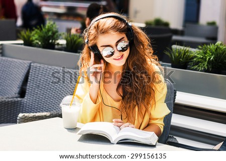 young beautiful woman sitting in a cafe drinking a milkshake reading a book and listening to music