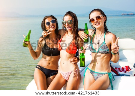 Three beautiful cheerful wet hipster girl at the beach on a tropical island, sitting on the speedboat, drink beer, merry company, sexy bikinis, sunglasses, crazy emotions, grimace, speed boat, sea